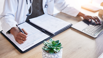 A doctor is seated at a desk, diligently writing on a clipboard